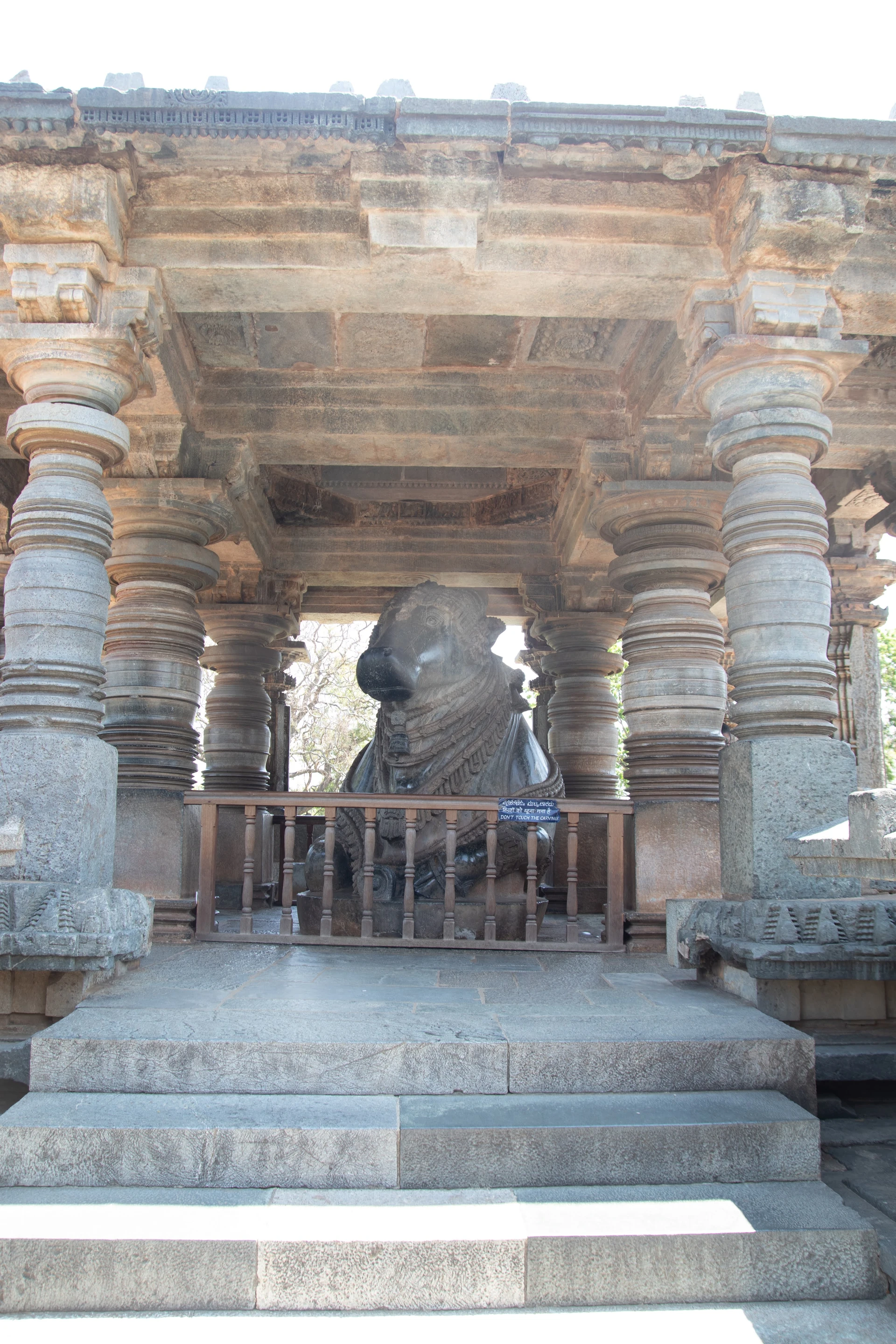Standing deity figure on Hoysaleswara Temple outer wall — upper register carved sculpture