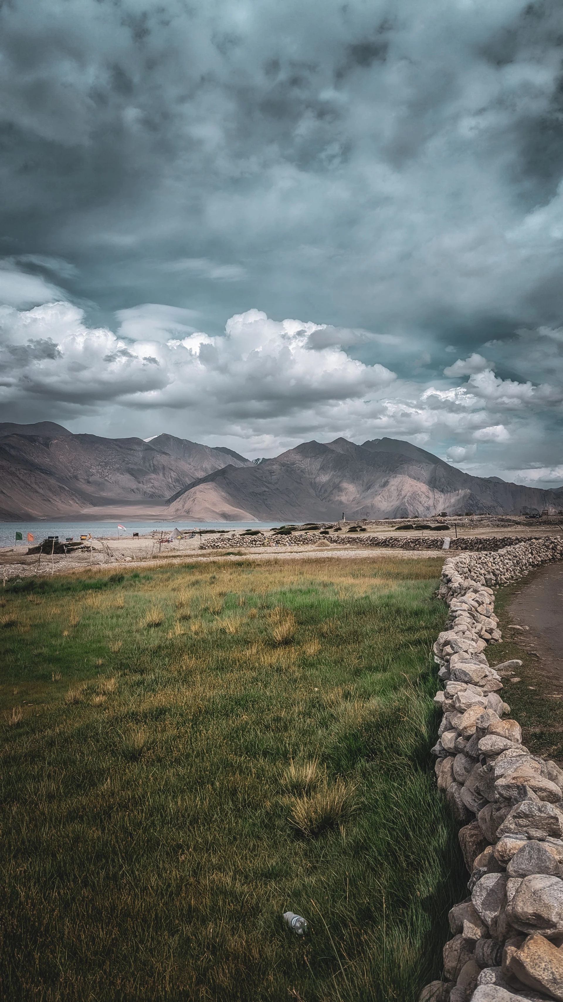 Green field with stone wall and storm clouds, Ladakh